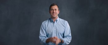 Movie still from “Operation Varsity Blues” (2021), directed by Chris Smith – A man wearing a blue shirt clapping his hands; Medium shot, Low angle