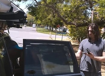 Movie still from “Operation Varsity Blues” (2021), directed by Chris Smith – A man standing in front of a car with another man standing next to it; Medium shot, Over the shoulder angle