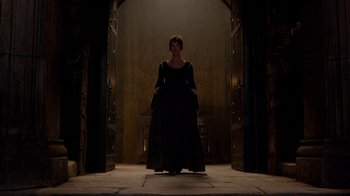 Movie still from “Outlander” (2014), created by Ronald D. Moore – A woman in a black dress standing in front of an open door; Wide shot, Low angle