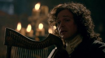Movie still from “Outlander” (2014), created by Ronald D. Moore – A man holding a harp in front of a chandelier; Close Up shot, Over the shoulder angle