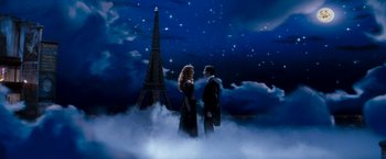 Movie still from “Moulin Rouge!” (2001), directed by Baz Luhrmann – A man and a woman standing next to each other in front of the eiffel tower at night; Wide shot, Low angle
