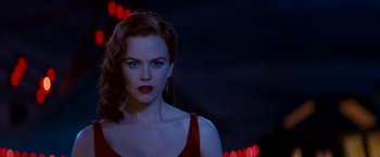 Movie still from “Moulin Rouge!” (2001), directed by Baz Luhrmann – A woman in a red dress is standing in front of lights at night; Close Up shot, Over the shoulder angle