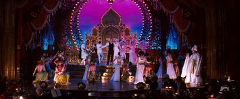 Movie still from “Moulin Rouge!” (2001), directed by Baz Luhrmann – A group of people standing on top of a stage in front of lights; Wide shot, High angle
