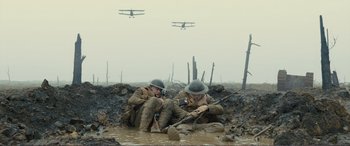 Movie still from “1917” (2019), directed by Sam Mendes – Two men in uniforms sitting in the mud with a plane in the background; Wide shot, High angle