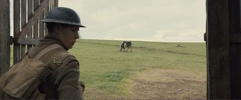 Movie still from “1917” (2019), directed by Sam Mendes – A man standing in a grassy field with a cow grazing; Medium shot, Over the shoulder angle