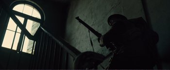Movie still from “1917” (2019), directed by Sam Mendes – A man holding a gun up to a railing in a dark room; Medium shot, Low angle