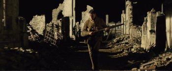 Movie still from “1917” (2019), directed by Sam Mendes – A man is walking through the ruins holding a rifle; Wide shot, Low angle