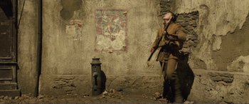 Movie still from “1917” (2019), directed by Sam Mendes – A man standing next to a fire hydrant in front of a wall; Wide shot, Low angle
