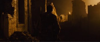 Movie still from “1917” (2019), directed by Sam Mendes – A man standing on a street at night with a backpack; Wide shot, Over the shoulder angle