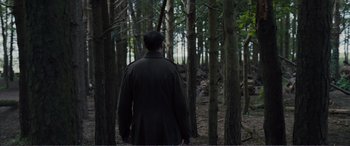 Movie still from “1917” (2019), directed by Sam Mendes – A man walking through the woods wearing a black coat; Wide shot, Low angle