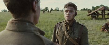 Movie still from “1917” (2019), directed by Sam Mendes – A man in a military uniform talking to another man in a grassy field; Close Up shot, Over the shoulder angle