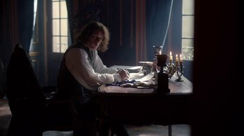 Movie still from “Outlander” (2014), created by Ronald D. Moore – A man sitting at a table writing on a piece of paper; Medium shot, Over the shoulder angle