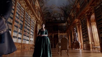 Movie still from “Outlander” (2014), created by Ronald D. Moore – A woman in a green dress standing in a library; Wide shot, Low angle