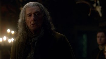 Movie still from “Outlander” (2014), created by Ronald D. Moore – An older man with long white hair is looking at the camera; Close Up shot, Over the shoulder angle