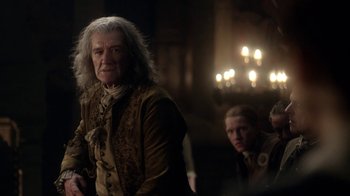 Movie still from “Outlander” (2014), created by Ronald D. Moore – A man with long white hair standing next to another man; Medium shot, Over the shoulder angle