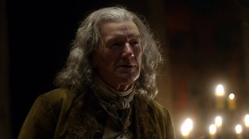 Movie still from “Outlander” (2014), created by Ronald D. Moore – An older man with long white hair is looking at the camera; Close Up shot, Low angle