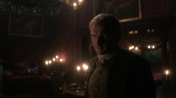 Movie still from “Outlander” (2014), created by Ronald D. Moore – A man standing in front of candles in a room; Close Up shot, Over the shoulder angle