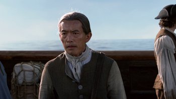 Movie still from “Outlander” (2014), created by Ronald D. Moore – An older man wearing a vest standing on a boat; Close Up shot, Over the shoulder angle