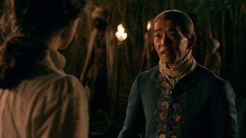 Movie still from “Outlander” (2014), created by Ronald D. Moore – An older man wearing a blue jacket and a scarf; Medium shot, Over the shoulder angle