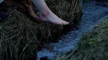 Movie still from “Outlander” (2014), created by Ronald D. Moore – A person's bare feet in the grass next to a stream; Extreme Close Up shot, High angle