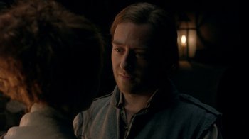 Movie still from “Outlander” (2014), created by Ronald D. Moore – A man with a beard is standing in a dark room; Close Up shot, Over the shoulder angle