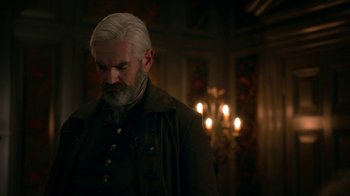 Movie still from “Outlander” (2014), created by Ronald D. Moore – An older man with white hair standing in front of candles; Medium shot, Over the shoulder angle
