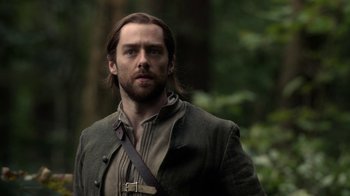 Movie still from “Outlander” (2014), created by Ronald D. Moore – A man with long hair and beard standing in the woods; Close Up shot, Over the shoulder angle