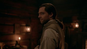 Movie still from “Outlander” (2014), created by Ronald D. Moore – A man with long hair standing in a dark room; Close Up shot, Over the shoulder angle