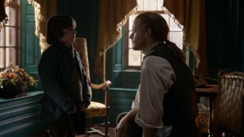 Movie still from “Outlander” (2014), created by Ronald D. Moore – A man and a boy are talking in a living room; Medium shot, Over the shoulder angle