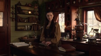 Movie still from “Outlander” (2014), created by Ronald D. Moore – A woman standing at a table in front of a book; Medium shot, Over the shoulder angle