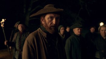 Movie still from “Outlander” (2014), created by Ronald D. Moore – A group of people in a dark forest; Medium shot, Over the shoulder angle