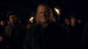 Movie still from “Outlander” (2014), created by Ronald D. Moore – A man in a black jacket and some people with torches; Medium shot, Low angle