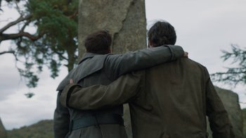 Movie still from “Outlander” (2014), created by Ronald D. Moore – Two men are hugging near a tree in a park; Medium shot, Low angle