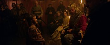 Movie still from “Outlaw King” (2018), directed by David Mackenzie – A group of people sitting in a room with a king; Medium shot, Over the shoulder angle