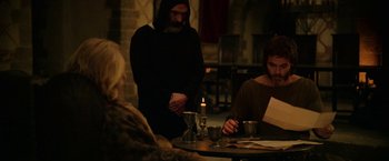 Movie still from “Outlaw King” (2018), directed by David Mackenzie – A group of people sitting around a table with a candle; Medium shot, Over the shoulder angle