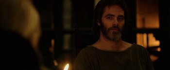 Movie still from “Outlaw King” (2018), directed by David Mackenzie – A man with long hair and a beard sitting in front of a lit candle; Close Up shot, Over the shoulder angle