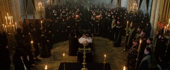 Movie still from “Outlaw King” (2018), directed by David Mackenzie – A large group of people in black robes standing in a room with candles; Wide shot, High angle