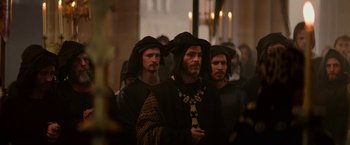 Movie still from “Outlaw King” (2018), directed by David Mackenzie – A group of men dressed in medieval garb in front of candles; Medium shot, Over the shoulder angle