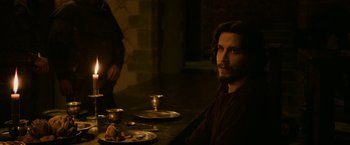 Movie still from “Outlaw King” (2018), directed by David Mackenzie – A man sitting at a table with plates of food on it; Medium shot, Over the shoulder angle