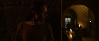 Movie still from “Outlaw King” (2018), directed by David Mackenzie – A woman standing next to a window in a dark room; Medium shot, Over the shoulder angle