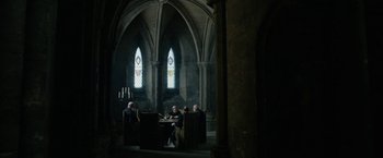 Movie still from “Outlaw King” (2018), directed by David Mackenzie – A group of people sitting around a table in front of a stained glass window; Wide shot, Low angle