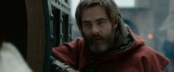 Movie still from “Outlaw King” (2018), directed by David Mackenzie – A man with long hair and a beard is leaning against a metal fence; Close Up shot, Over the shoulder angle