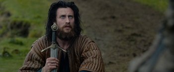 Movie still from “Outlaw King” (2018), directed by David Mackenzie – A man with long hair holding a sword in his hand; Close Up shot, Over the shoulder angle