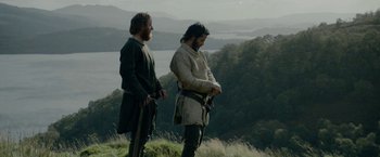 Movie still from “Outlaw King” (2018), directed by David Mackenzie – Two men standing on top of a hill looking at a body of water in the distance; Medium shot, Low angle