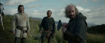 Movie still from “Outlaw King” (2018), directed by David Mackenzie – Two men are standing in a field with an axe; Medium shot, Over the shoulder angle