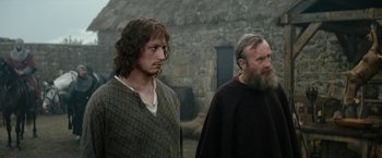 Movie still from “Outlaw King” (2018), directed by David Mackenzie – Two men standing next to each other near a stone wall; Medium shot, Low angle