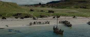 Movie still from “Outlaw King” (2018), directed by David Mackenzie – A group of people walking on the beach near a boat; Extreme Wide shot, High angle