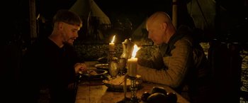 Movie still from “Outlaw King” (2018), directed by David Mackenzie – Two men are sitting at a table with candles; Medium shot, Over the shoulder angle
