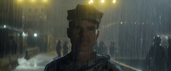 Movie still from “Outside the Wire” (2021), directed by Mikael Håfström – A man wearing a hat standing in the pouring rain; Close Up shot, Low angle