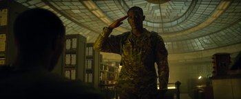 Movie still from “Outside the Wire” (2021), directed by Mikael Håfström – A soldier saluting while wearing a uniform in a building; Medium shot, Low angle